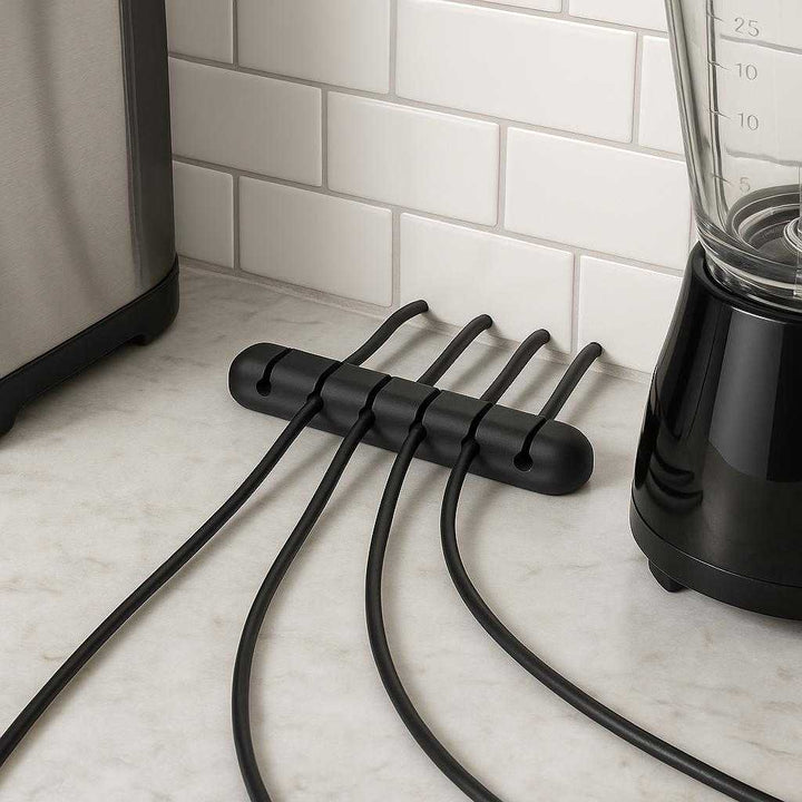 Ledningsholder i moderne design - Perfekt til skrivebord og køkkenapparater, Sort: A different realistic kitchen counter setting where the product is securely positioned on a marble countertop, being used to neatly organize various appliance cords like a toaster and blender.
