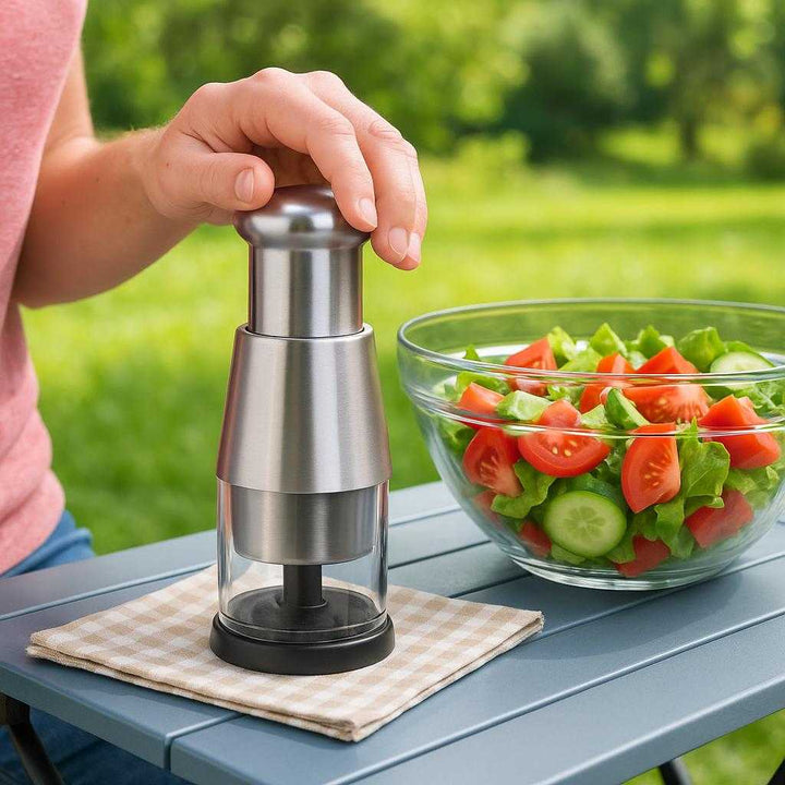 Løghakker med Effektiv Trykhakker og Beholder - Kompakt Design i Sort og Sølv: A different realistic picnic setting where the product is securely positioned on a portable outdoor table, being used to prepare a fresh salad.