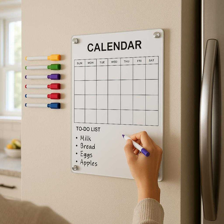 Magnetisk Vægkalender i Glas - Elegant og Praktisk til Hjemmet eller Kontoret, Tilgængelig i Stor og Lille Størrelse: A realistic modern kitchen setting where the small glass magnetic calendar is properly grounded on a light-colored wall near a refrigerator, being actively used by a person writing with a colorful marker.