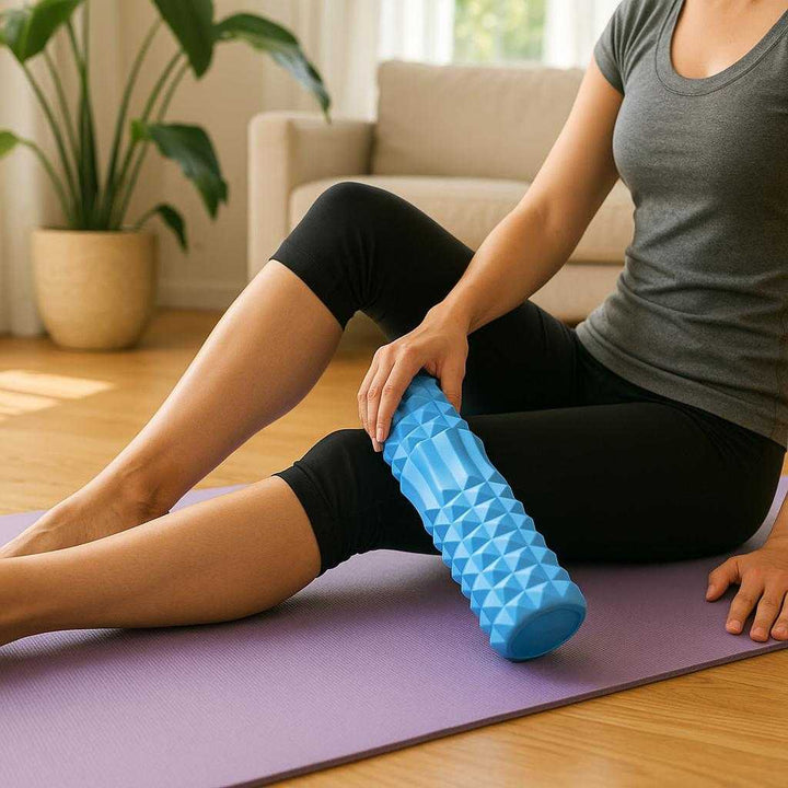 Massagerulle med Dybdegående Struktur i Blå, Lilla, Lyserød, Sort – Professionel Restitution & Komfort. A person uses the blue textured massage roller on their leg muscles, sitting on a yoga mat in a bright, airy living room with sunlight streaming in and plants nearby.
