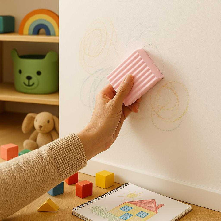 Melaminsvamp - Effektiv Rengøring uden Kemikalier i Lysegrå, Lyserød og Gul. In a children's playroom, the melamine sponge in its lyserød variation is seen used by an adult to clean crayon marks off a white wall. The setting is colorful and lively, with toy blocks and a child's drawing book scattered around. Soft, ambient lighting enhances the family-friendly environment, demonstrating the sponge's gentle yet powerful cleaning ability without harsh chemicals.