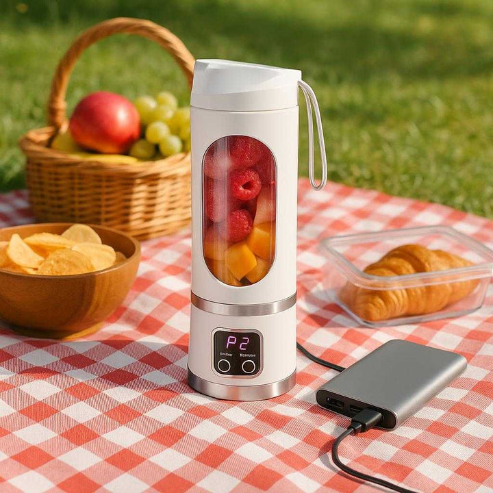 Miniblender med LCD-display - Bærbar, Genopladelig og Moderne Design i Hvid og Sølv: A different realistic outdoor picnic scene where the miniblender is securely positioned on a checkered picnic blanket, being naturally placed among packed snacks and a fruit basket.