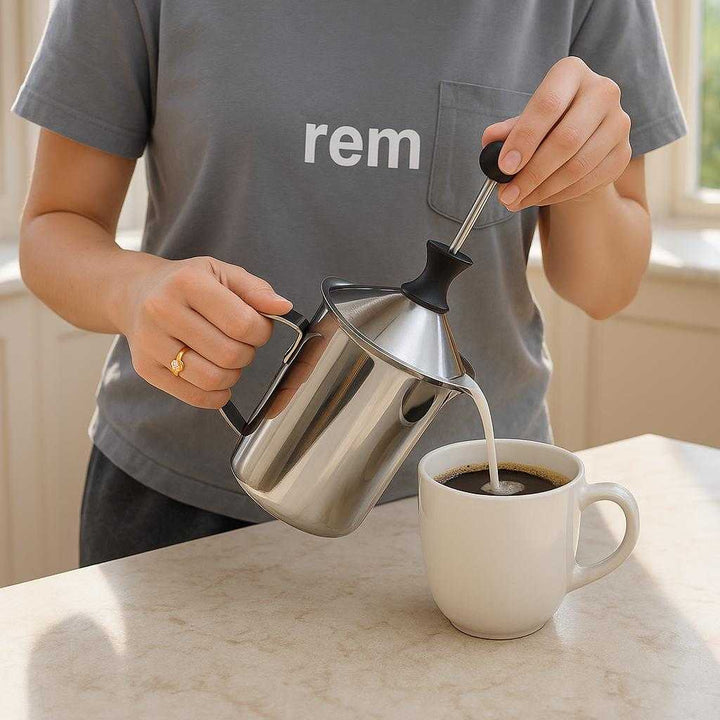 Mælkeskummer i sølvfarvet rustfrit stål, plastik og solid konstruktion - let at bruge, hurtig skumning, holdbar: A realistic kitchen counter setting where the mælkeskummer is properly grounded on a marble countertop, being actively used by someone wearing casual home attire.