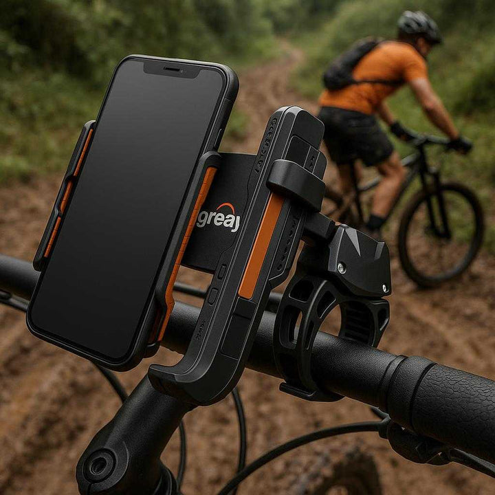 Mobilholder til Cykel - Justerbar og Stødabsorberende Sort Design med Orange Detaljer. The adjustable and shock-absorbing black bike phone holder with orange details securely grips a smartphone on a mountain bike handlebars, with a cyclist navigating a rugged, muddy trail in the background.
