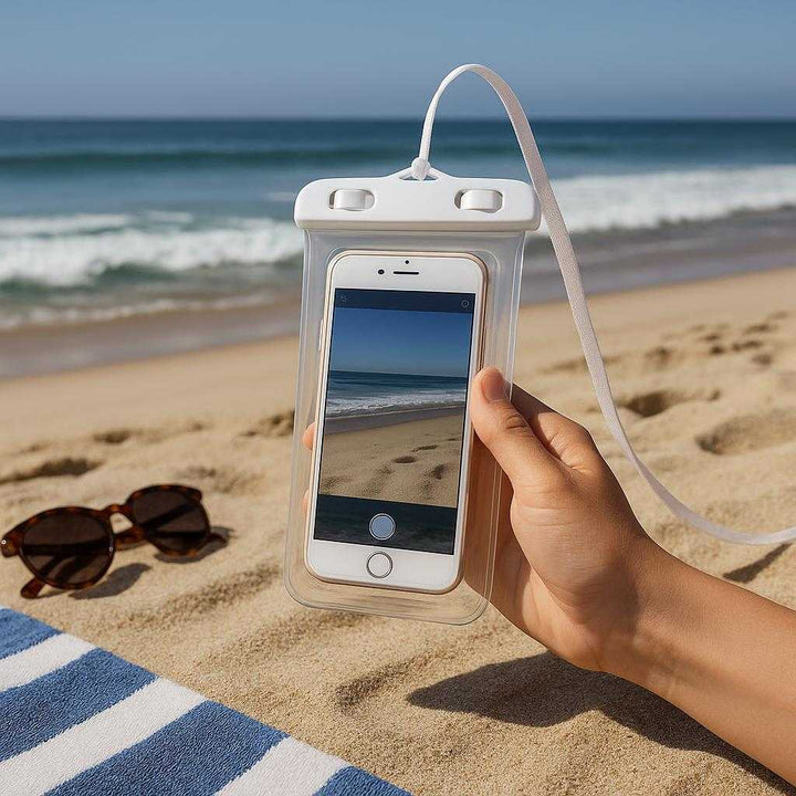 Mobilpose - Vandtæt og Touch-venlig, Perfekt til Svømning & Strand, Tilgængelig i 8 Farver: A realistic beach setting where the waterproof phone pouch is properly grounded in the sand beside a beach towel, actively being used by a person to take photos of the ocean.