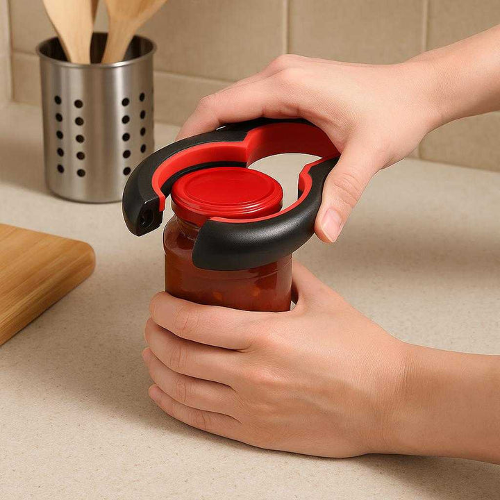 Multiåbner til Nem Åbning af Flasker og Dåser i Sort og Rød - Ergonomisk Design med Høj Kvalitet: A realistic kitchen countertop setting where the multi-opener is properly grounded on the counter, being actively used by hands to open a jar, with natural lighting casting realistic shadows and showing clear contact points where the product touches the surface.