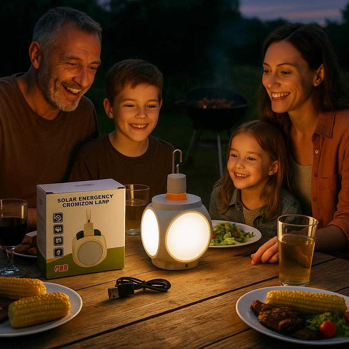 Nødlommelygte med solcelle - Bærbar, energibesparende lyskilde til udendørs og nødsituationer. On a wooden picnic table during a family barbecue at dusk, the solar emergency lamp casts a warm glow over the tabletop, surrounded by smiling faces enjoying their meal.