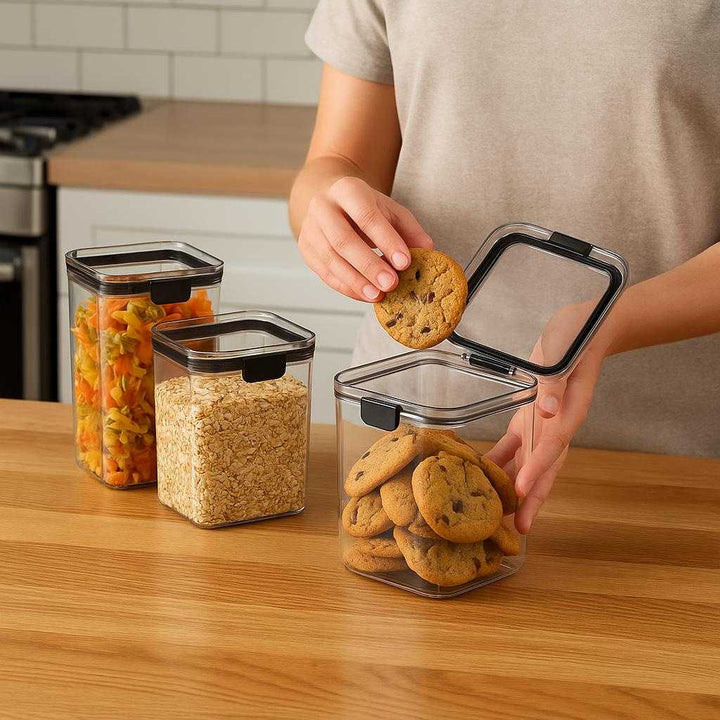 Opbevaringsbøtter til Køkkenet – Professionel, Høj Kvalitet, Lufttæt Opbevaring 460ml-1300ml: A realistic modern kitchen setting where the product is properly grounded on a wooden countertop, being actively used by a person to store freshly baked cookies into one container, with natural lighting casting realistic shadows and showing clear contact points where the product touches the countertop.