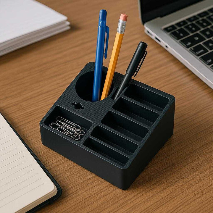 Opbevaringsholder i Sort Plast med Flerdelt Ruminddeling - Professionel Høj Kvalitet til Kontor og Hjem. The black plastic organizer is placed on a busy office desk, holding pens, pencils, and paper clips, with a laptop and a notebook visible nearby.