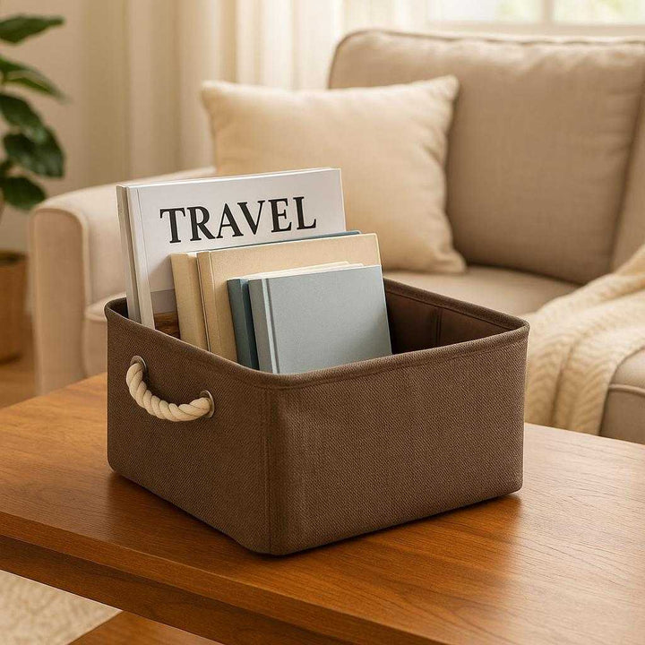 Opbevaringspose i kraftigt stof med snøre – Foldbar og slidstærk løsning til hjem og rejse i brun, beige og grå: A realistic cozy living room where the storage bag is properly grounded on a wooden coffee table, being actively used to organize and hold a collection of magazines and books, with natural lighting casting realistic shadows and showing clear contact points where the product touches the table surface, surrounded by a warm and inviting home environment.