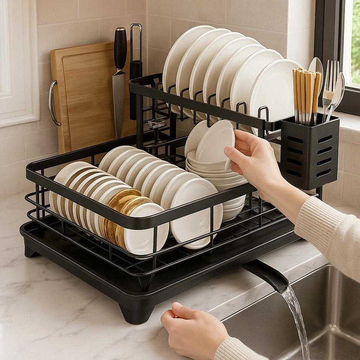 Opvaskestativ i stål med to niveauer – Sort og hvid variant til rådighed med effektiv tørring og organiseret opbevaring: A realistic kitchen countertop setting where the product is properly grounded on a marble surface, being actively used with plates, glasses, and utensils neatly organized on it by a person’s hands.