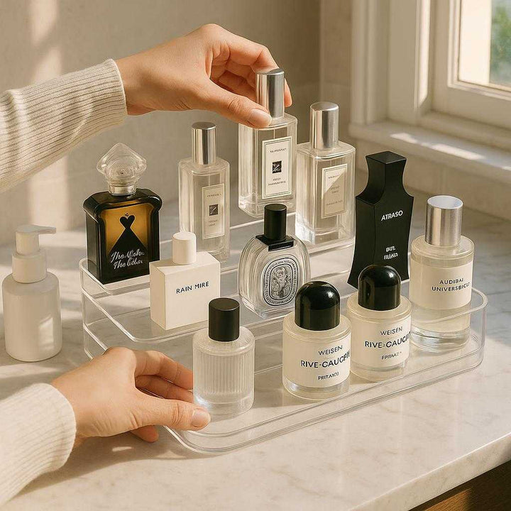 Organizer i Klar Akryl med 3 Niveauer til Makeup - Stilfuld og Praktisk Opbevaringsløsning: A realistic bathroom vanity setting where the product is properly grounded on a marble countertop, being actively used by a person organizing various skincare bottles into it, with natural lighting streaming through a nearby window, casting realistic shadows and showing clear contact points where the product and bottles touch the surface.