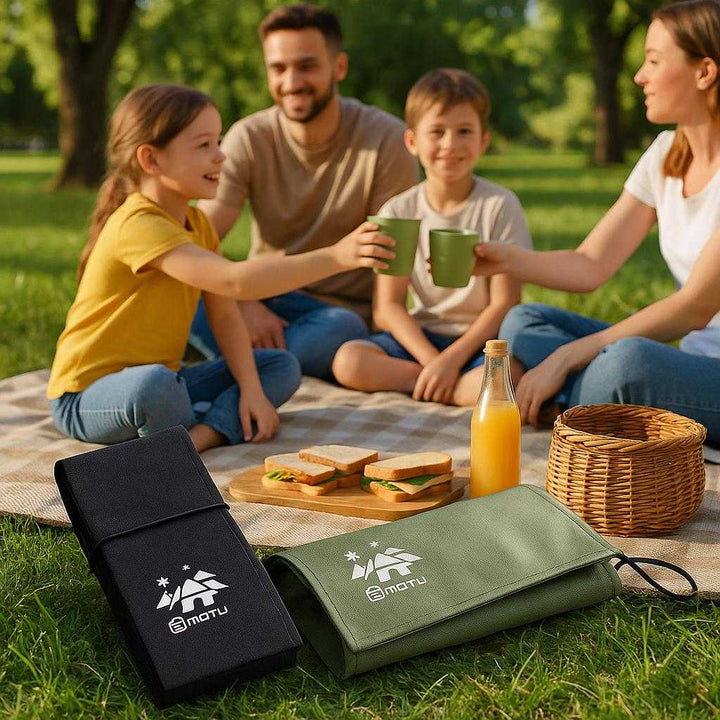 Picnic Tæppe: Vandtæt, Letvægt, Sammenklappeligt - Ideel til Udendørs Aktiviteter i Grøn og Sort Farve: A realistic park setting where the picnic blanket is properly grounded on a grassy area, being actively used by a family enjoying a sunny day.
