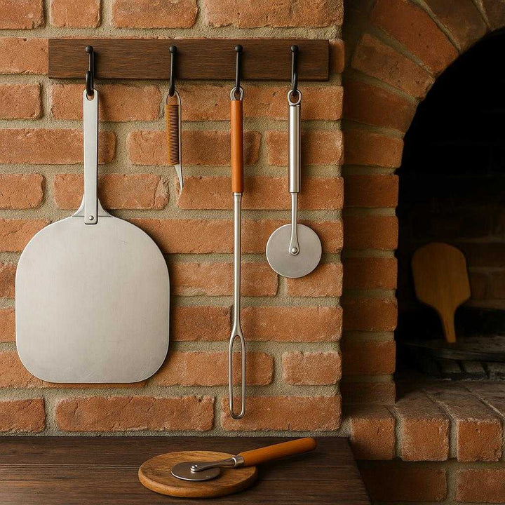 Pizzabørste i rustfrit stål og træskaft – Professionel og Høj Kvalitet til Pizzaovn. The pizza brush with a wooden handle hangs stylishly on a rack in a rustic outdoor kitchen, surrounded by brick walls and an array of pizza-making tools.