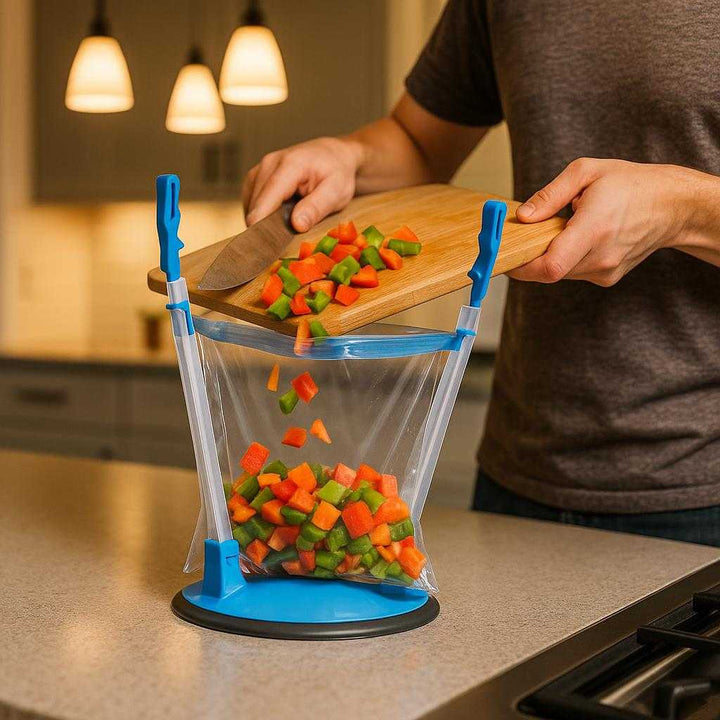 Plastikposeholder med justerbare arme og robust sugekop - Tilgængelig i Blå, Sort og Grøn. The adjustable bag holder is secured to a sleek kitchen counter, holding a bag open as a home chef effortlessly pours freshly chopped vegetables inside, under the warm glow of pendant lights.
