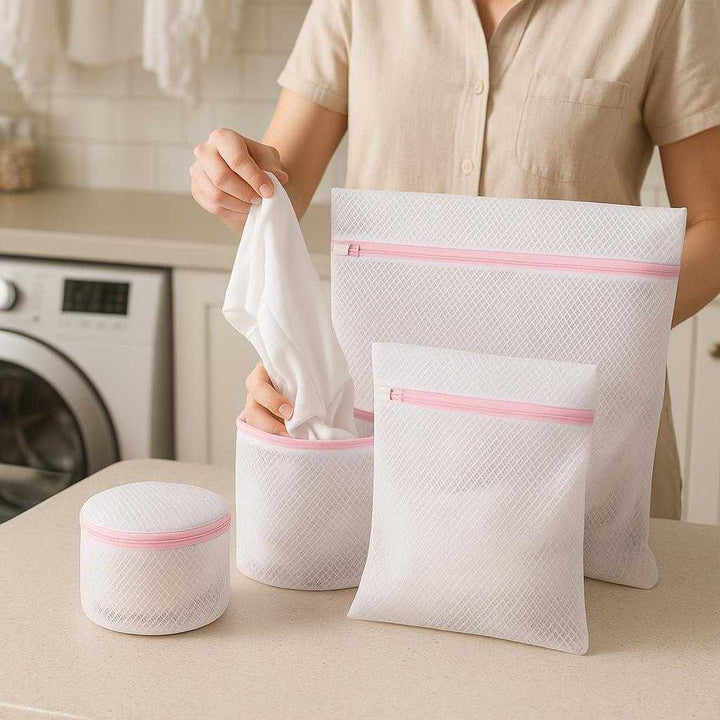 Polyester vasketøjsnet poser - 4 stk. net stofmateriale og plastik lynlås - hvid og lyserød: A realistic laundry room setting where the polyester laundry bags are properly grounded on a light-colored countertop, being actively used by a person who is sorting delicate clothing items into the bags.