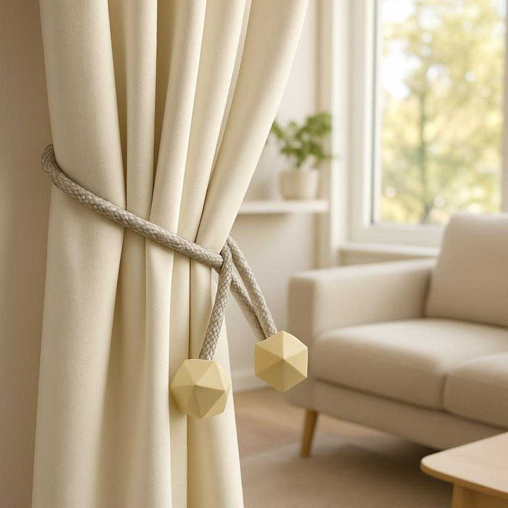 Professionel Gardinholder i Sølv og Beige - Magnetisk og Fleksibel Løsning med Geometriske Ender. The magnetic and flexible curtain holder elegantly secures a light vanilla-colored curtain with its geometric ends, framing a sunlit window in a modern living room.