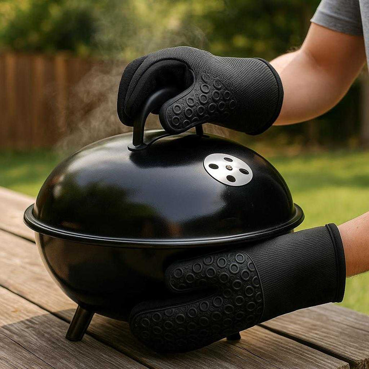 Professionel Grydelap i Silikone og Stof - Høj Kvalitet og Varmeresistens til Sikker Madlavning: A different realistic barbecue setting where the silicone and fabric oven mitt is securely positioned on a picnic table beside a grill, being used differently to confidently handle a hot grill lid.