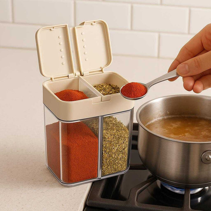 Professionel Krydderibøtte med Dobbelt Låg, Transparent Beholder og Høj Kvalitet. The transparent spice container with a double lid sits open on a kitchen counter filled with colorful spices, as a person measures out a spoonful next to a simmering pot.