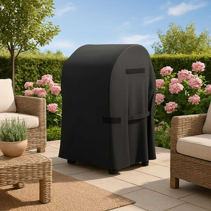 Professionel Overtræk til Grill - Vandtæt, Slidstærkt og Stilfuldt i Sort Design. A stylish backyard setting with the black grill cover neatly placed over the grill, surrounded by outdoor furniture and blooming plants, under a clear blue sky.