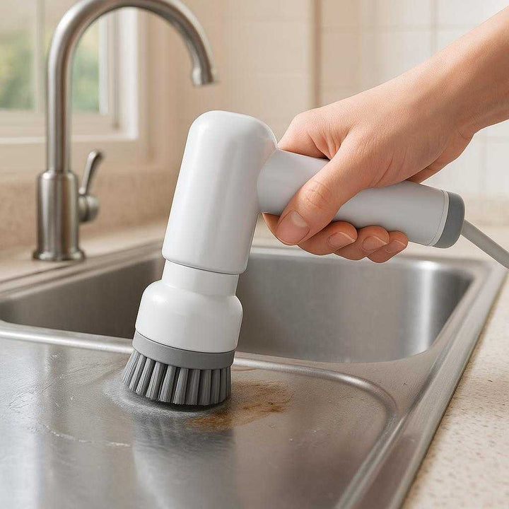 Rengøringsbørste Grå Elektrisk – Genopladelig med 4 Hoveder, Professionel og Høj Kvalitet: A realistic kitchen setting where the Rengøringsbørste Grå Elektrisk is properly grounded on a countertop, being actively used by a person's hand to scrub the surface of a stainless steel sink.