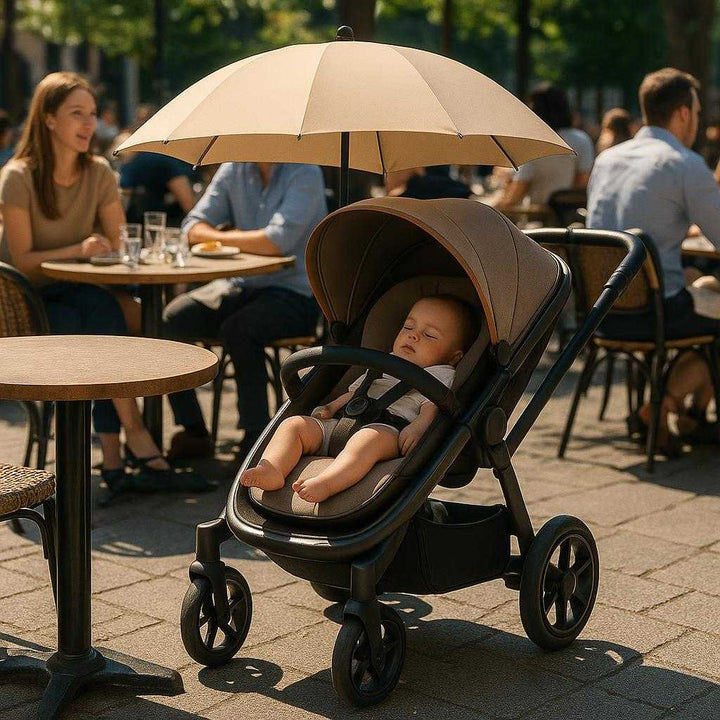 Rullebord 'Paraply' = 'Paraply' i metal, Tekstil og Plastik - Beskytter mod Sol, Komfortabel Siddeplads - Pink, Beige, Tågeblå, Grøn: A different realistic setting of a sunny outdoor cafe where the stroller with umbrella is securely positioned next to a table, with the umbrella providing shade to a child peacefully napping inside, surrounded by people enjoying their meals, with proper physics, shadows, and realistic integration into the lively environment.