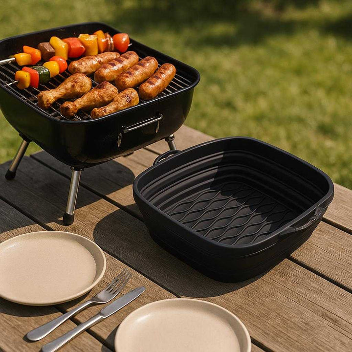 Sammenklappelig Airfryer Silikoneform Firkantet - Effektiv Madlavning, Fleksibel Design, Høj Kvalitet: A different realistic outdoor picnic area where the Sammenklappelig Airfryer Silikoneform Firkantet is securely positioned on a picnic table, being naturally placed next to a portable grill with cooked food displayed inside it, inviting guests to serve themselves.