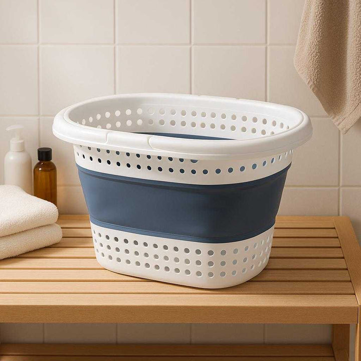 Sammenklappelig vasketøjskurv i plast og silikone – Let, rummelig og pladsbesparende i blå og hvid: A different realistic bathroom setting where the collapsible laundry basket is securely positioned on a wooden bench, naturally placed as part of an organized laundry setup with towels and toiletries nearby.