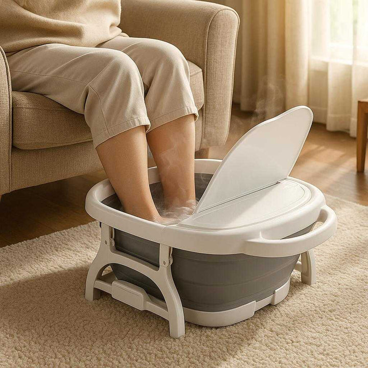 Sammenklappeligt Fodbad – Foldbart Spa-Kar med Massage & Låg i Høj Kvalitet: A realistic living room setting where the Foldable Foot Bath is properly grounded on a plush carpet, being actively used by a person seated in a cozy armchair, their feet immersed in warm, steaming water inside the bath.