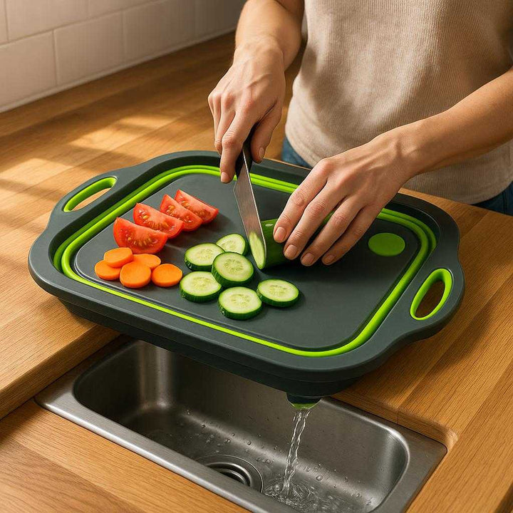 Sammenklappeligt skærebræt med afløb og håndtag – Multifunktionelt og Pladsbesparende Design i Moderne Grå og Lysegrøn: A realistic kitchen setting where the product is properly grounded on a wooden countertop, being actively used by a person slicing fresh vegetables with a sharp knife, with natural lighting casting realistic shadows and showing clear contact points where the cutting board touches the countertop, and water draining through the board's integrated drain feature into a sink below.