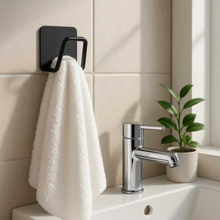 Selvklæbende vægkrog i mat sort metal - Moderne og pladsbesparende ophæng til hjemmet: A realistic bathroom setting where the selvklæbende vægkrog i mat sort metal is properly grounded on a smooth, tiled wall, holding a fluffy white towel.