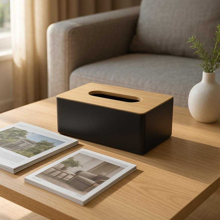 Servietboks i moderne design - Praktisk og æstetisk opbevaring til servietter i sort, lyserød, mørkeblå og hvid: A realistic modern living room setting where the serviet box is properly grounded on a sleek wooden coffee table, naturally placed among magazines and a decorative vase, with natural sunlight streaming through a nearby window, casting soft shadows and showing clear contact points where the product touches the table surface.