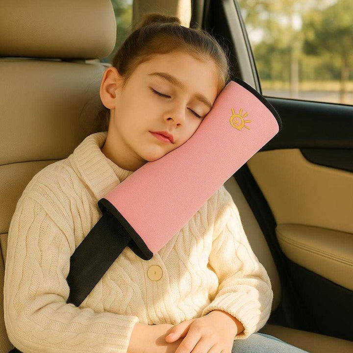 Sikkerhed Skulder Beskytter i Mikrofiber og Polstring - Beige, Grå, Blå, Lyserød: A realistic car interior setting where the Sikkerhed Skulder Beskytter in pink is properly grounded on a car seatbelt, actively used by a child sitting comfortably in the back seat.