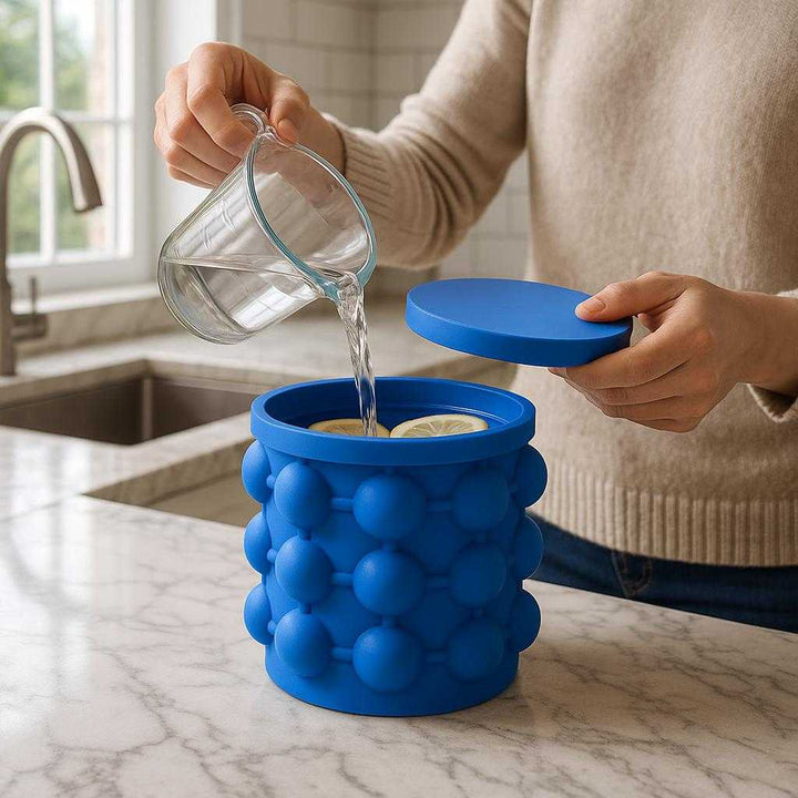 Silikone Isspand med Koboltblå Nuancer - Kompakt Design & Fødevaregodkendt Materiale: A realistic modern kitchen setting where the Silikone Isspand med Koboltblå Nuancer is properly grounded on a marble countertop, being actively used by a person filling it with water and adding lemon slices.