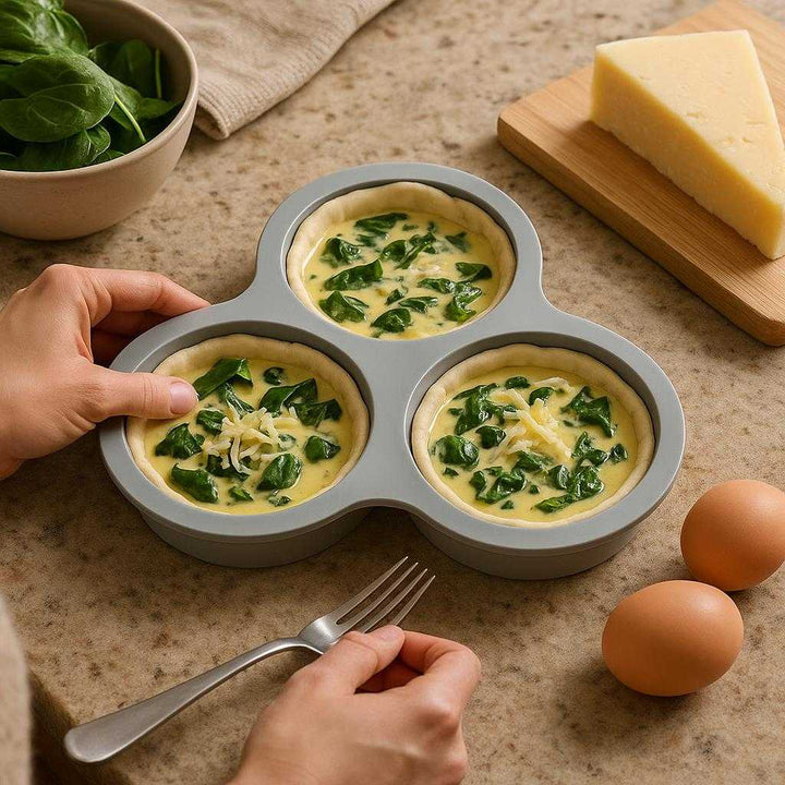 Silikoneform til Airfryer og Mikroovn - Høj Kvalitet, Foldbar, Grå, 80g: A realistic kitchen setting where the silicone form is properly grounded on a countertop, being actively used by a person to prepare small quiches for baking, with natural lighting casting realistic shadows and showing clear contact points where the form touches the countertop.