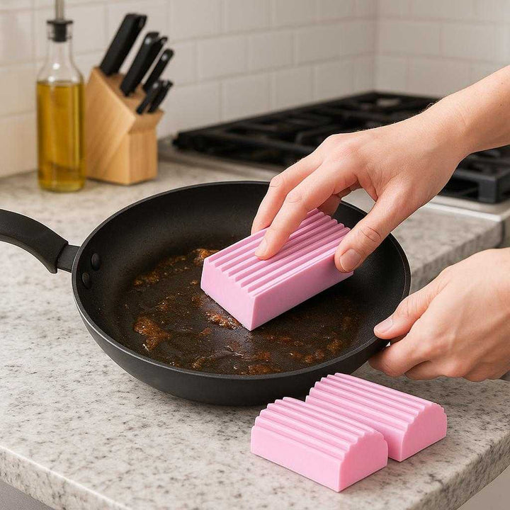 Silikonesvampe - 4 stk. Genanvendelige og Hygiejniske Svampe til Effektiv Rengøring i Hjemmet: A realistic kitchen setting where the product is properly grounded on a kitchen counter, being actively used by hands to scrub a frying pan, with natural lighting casting realistic shadows and showing clear contact points where the product touches the counter.