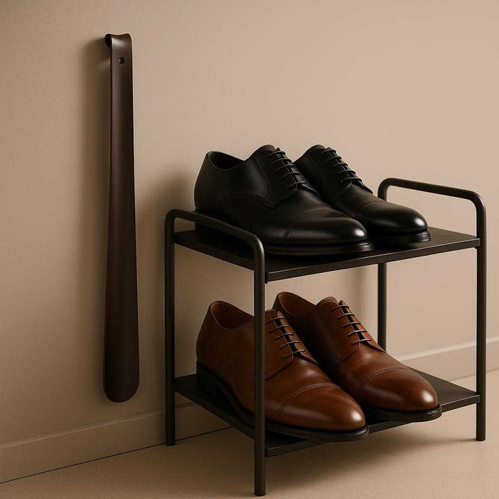 Skohorn i Sort Stål - Langt, Elegant og Funktionelt Design til Hverdagsbrug. The Skohorn i Sort Stål is displayed on a modern shoe shelf alongside polished shoes, with soft lighting highlighting its sleek design and functionality in a minimalist decor setting.