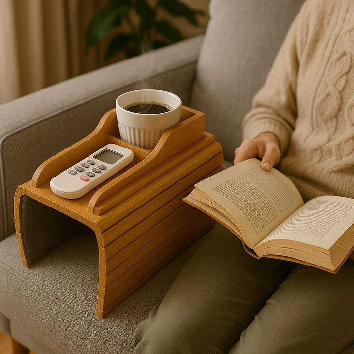 Sofabordbakke i Vintage Bambus – Elegant og Praktisk Design med Høj Kvalitet. The vintage bamboo sofa tray sits elegantly on a stylish home sofa armrest, holding a steaming cup of coffee and a remote control while a person relaxes with a book nearby.