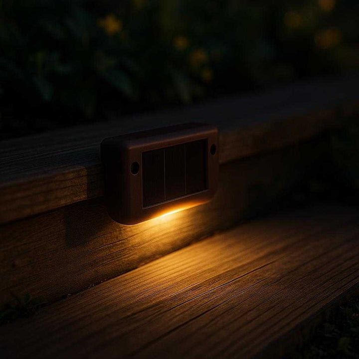 Solcelle Trappelys - LED Udendørslamper med Automatisk Sensor til Trapper og Hegn i Sort og Mørke Brun: A realistic outdoor garden setting at dusk, where the solar stair light is properly grounded on the edge of a wooden deck step, being naturally placed to illuminate the pathway.