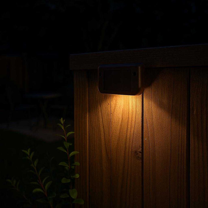 Solcelle Trappelys - LED Udendørslamper med Automatisk Sensor til Trapper og Hegn i Sort og Mørke Brun: A different realistic backyard fence setting during nighttime, where the solar light is securely positioned on the wooden fence, being used to softly light up the border of the yard.
