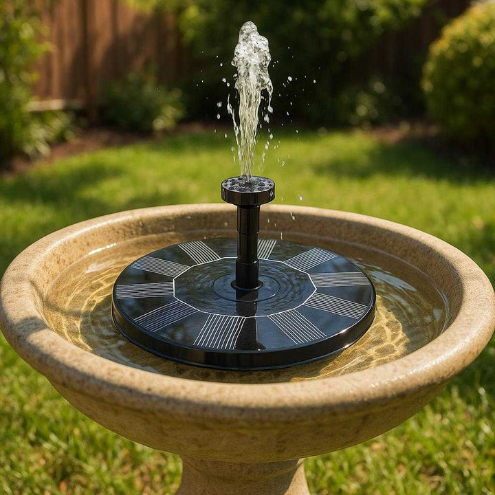 Solfontæne – Øko-venlig og solcelledrevet springvandspumpe til haven med udskiftelige dyser: A realistic garden setting where the solar-powered fountain pump is properly grounded in a birdbath, actively used with water gently cascading down in a sunny backyard.