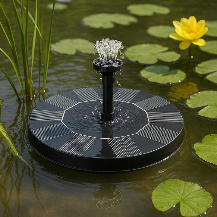 Solfontæne – Øko-venlig og solcelledrevet springvandspumpe til haven med udskiftelige dyser: A different realistic pond setting where the fountain pump is securely positioned on the water's surface amidst aquatic plants, creating a serene water display.