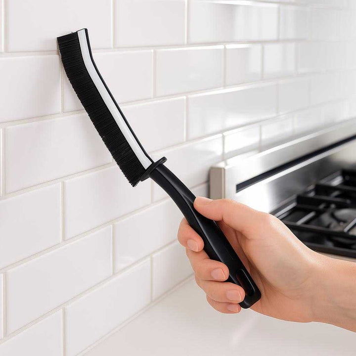 Sprækkebørste i sort og hvidt design - Effektiv til rengøring af smalle områder: A modern kitchen setting, where the product is efficiently cleaning grout lines between glossy white tiles on a kitchen backsplash.
