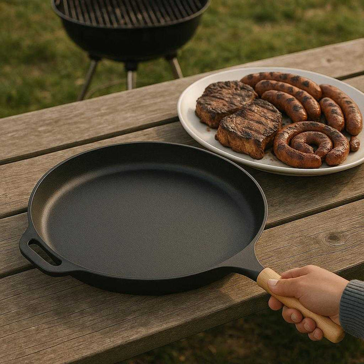 Støbejern Grillplade Sort - Jævn Varmefordeling, Holdbar, Ovnfast: A different realistic outdoor barbecue setting where the Støbejern Grillplade Sort is securely positioned on a picnic table, naturally placed beside a serving platter with grilled meats.