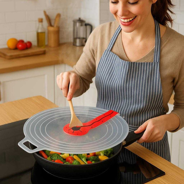 Stænklåg til pande og stegepande - Gennemsigtig silikone med rød detalje, varmebestandig og nem at rengøre. The silicone lid is securely placed over a sizzling pan on a modern stove, with steam gently rising and a cheerful cook stirring a vibrant stir-fry, showcasing its practicality in a lively kitchen environment.