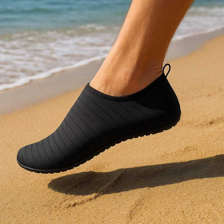 Strandsokker tilbehør - Skridsikre badesokker til strand og vandaktiviteter: A realistic beach setting where the sock is properly grounded on warm sand, being actively used by a person walking along the shoreline.
