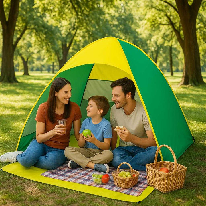 Strandtelt med UV-beskyttelse og nem opsætning i Grøn, Blå, Lyserød - Professionel og Vindmodstand. A family enjoys a picnic under the protective canopy of the green and yellow tent in a lush park, with trees casting dappled sunlight on the ground.