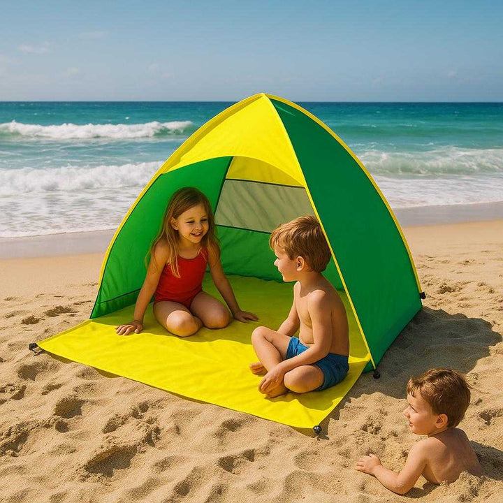 Strandtelt med UV-beskyttelse og nem opsætning i Grøn, Blå, Lyserød - Professionel og Vindmodstand. The vibrant green and yellow beach tent is set up on a sunny coastline, with children playing nearby under its shade and waves crashing in the background.