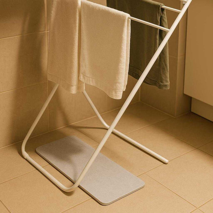 Vandabsorberende Stenmåtte – Kompakt Hurtigttørrende Bademåtte i Lys Grå til Badeværelset: A different realistic laundry room setting where the Vandabsorberende Stenmåtte is securely positioned beneath a clothes drying rack.