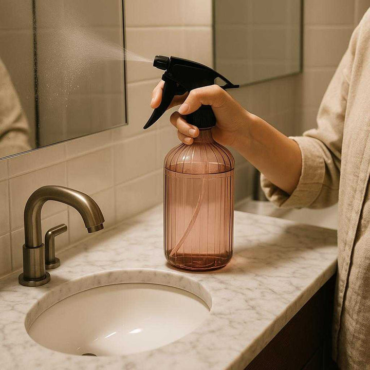 Vandkande i Plastik, Gennemsigtig, Let at Bruge, Justerbar Spray, God Kvalitet - Pink, Grøn, Grå 500ml: A different realistic cleaning scenario in a bathroom where the product is securely positioned on a marble counter next to a sink, being used by a person spraying a mirror.